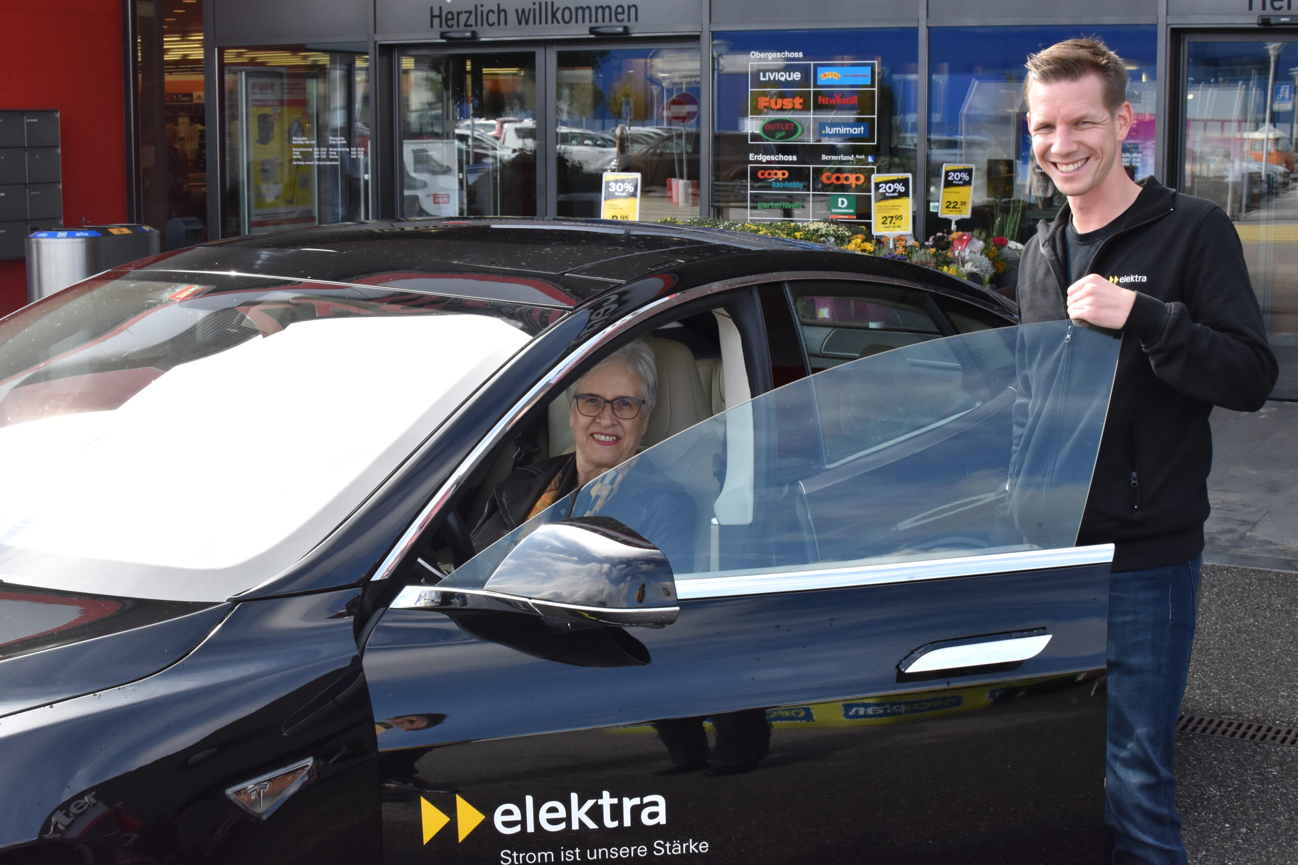 Die glückliche Gewinnerin der Mobility Week 2020 sitzt im Tesla und strahlt um die Wette mit dem Fachspezialisten für Energielösungen, Matthias Ostermeier.