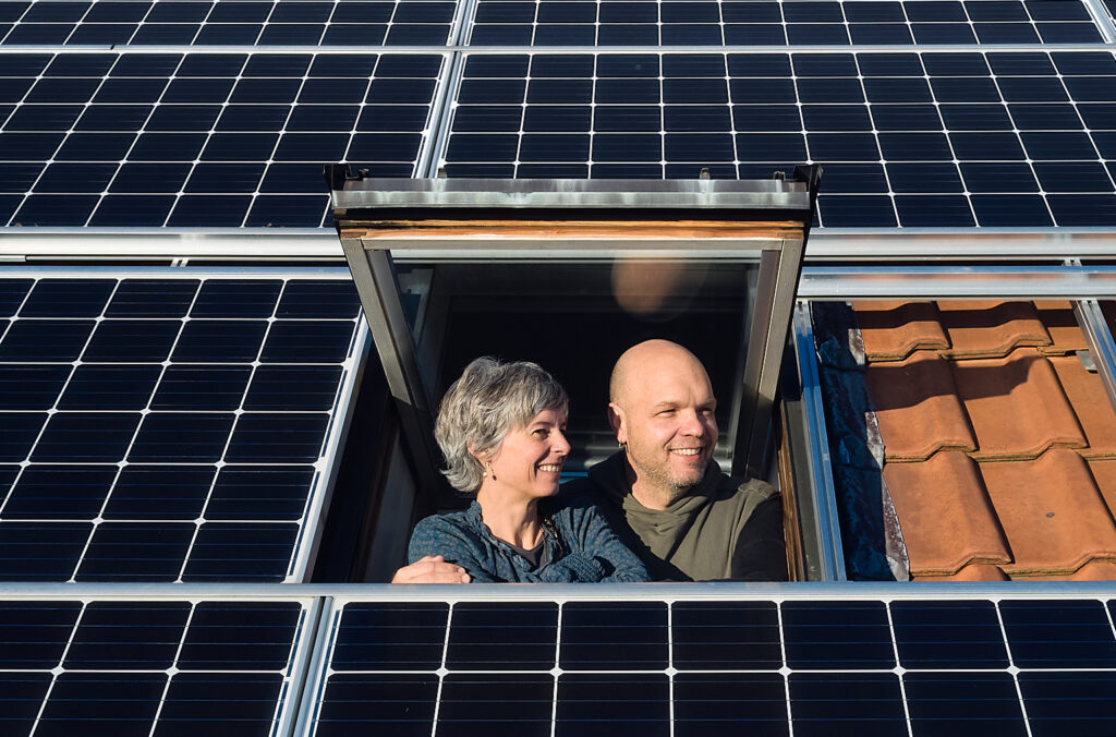 Isabelle und Lukas Loosli blicken aus dem Dachfenster, rund um sie sieht man die Panels der Solaranlage