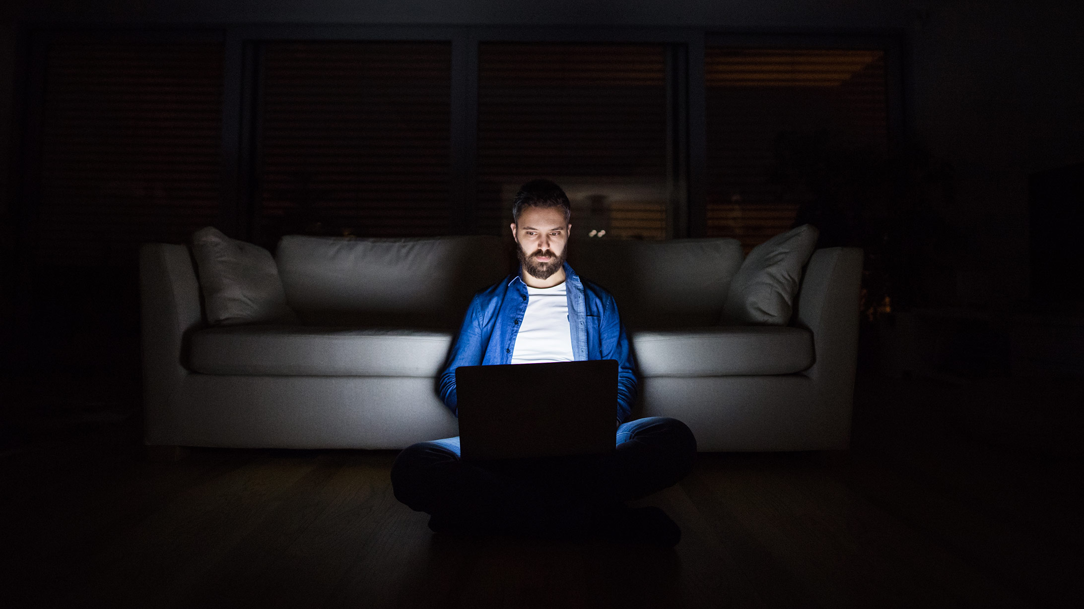 ein mann sitzt im dunkeln, sein laptopt ist die einzige lichtquelle