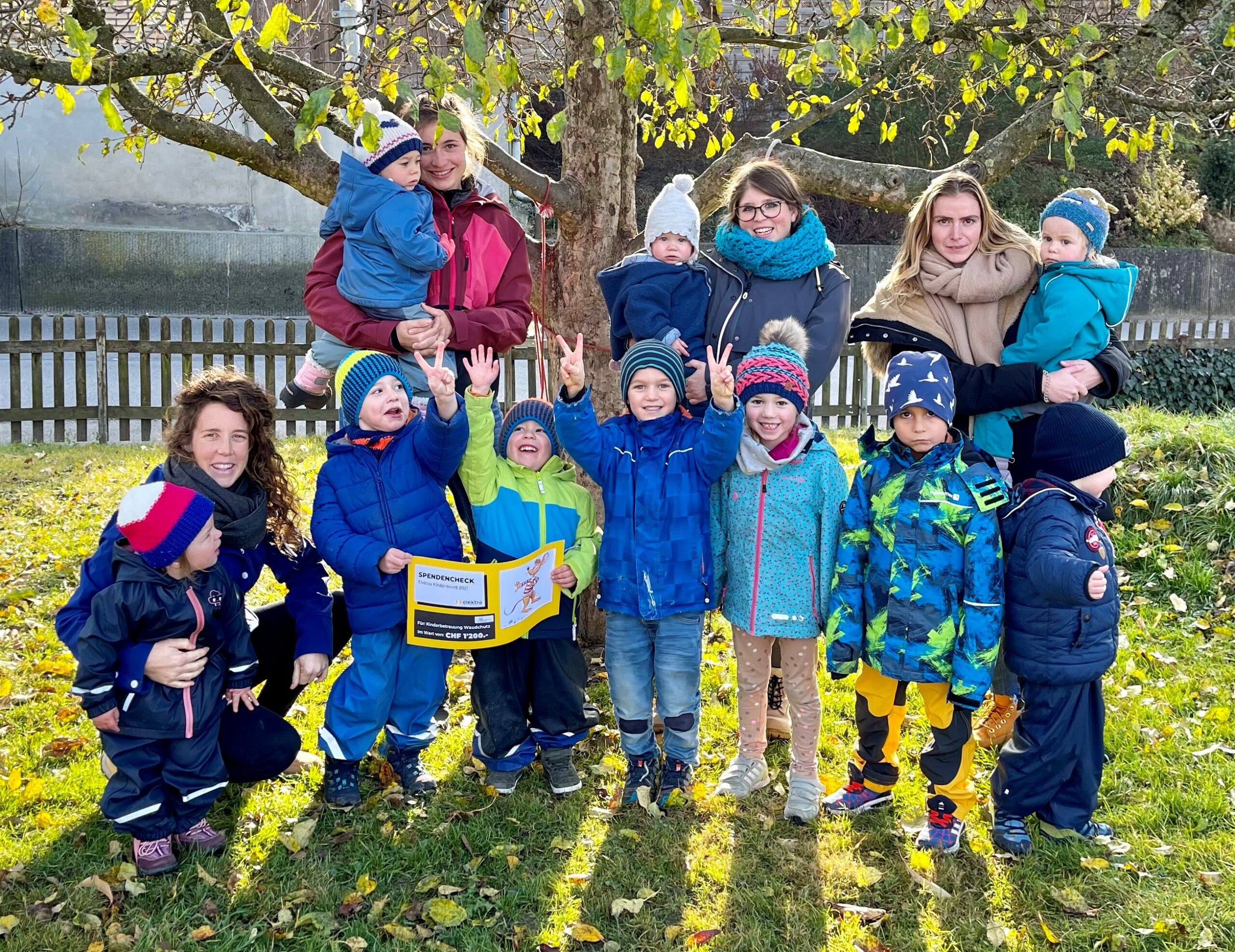 Die Kinder und Leiterinnen der Kinderbetreuung Waudchutz freuen sich über die grosszügige Spende des Elektra Kinderevents. Geplant ist eine Gartenverschönerung, weshalb sie auch gleich alle warm eingepackt in Winterjacken und Kappen im Garten posieren.